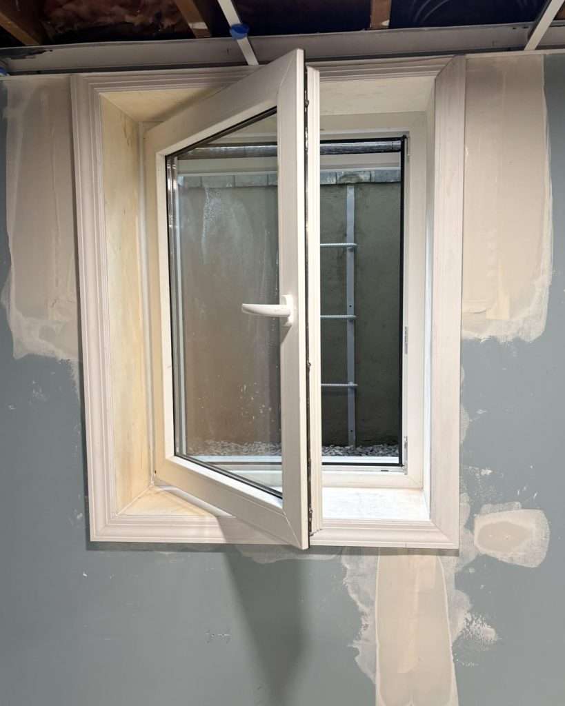 Open casement egress window in a basement wall with the window well ladder visible outside