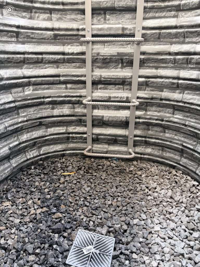 Inside a Boman Kemp stacked stone egress window well showing the ladder, drainage stone and drain on Long Island, NY