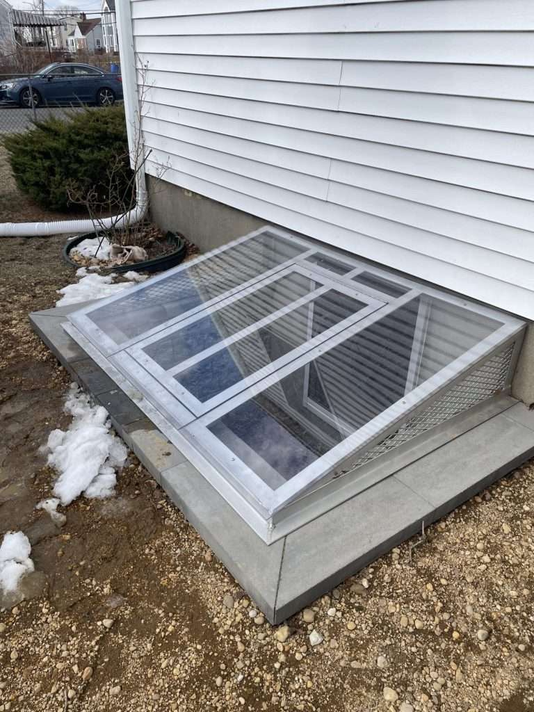 Clear polycarbonate egress window well cover with an aluminum frame over a basement window well on Long Island, NY
