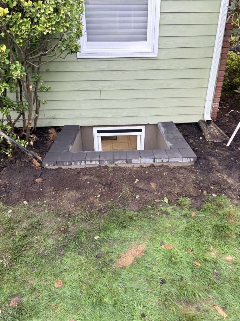 Completed masonry egress window well with paver caps in a front yard on Long Island, NY