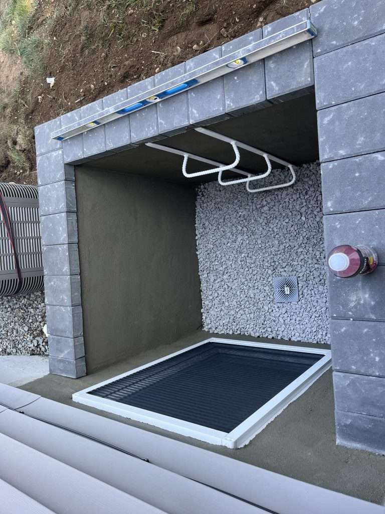Inside a block-built masonry egress window well showing the ladder, drainage stone and floor drain on Long Island, NY